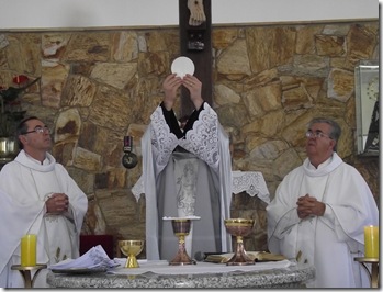 A imagem demonstra o sacerdote e ao seu lado lado os ministros extraordinários. 